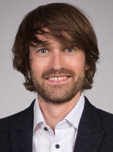 Tobias Meng mit mittellangem Haar und Bart, freundlich lächelnd vor hellem Hintergrund.